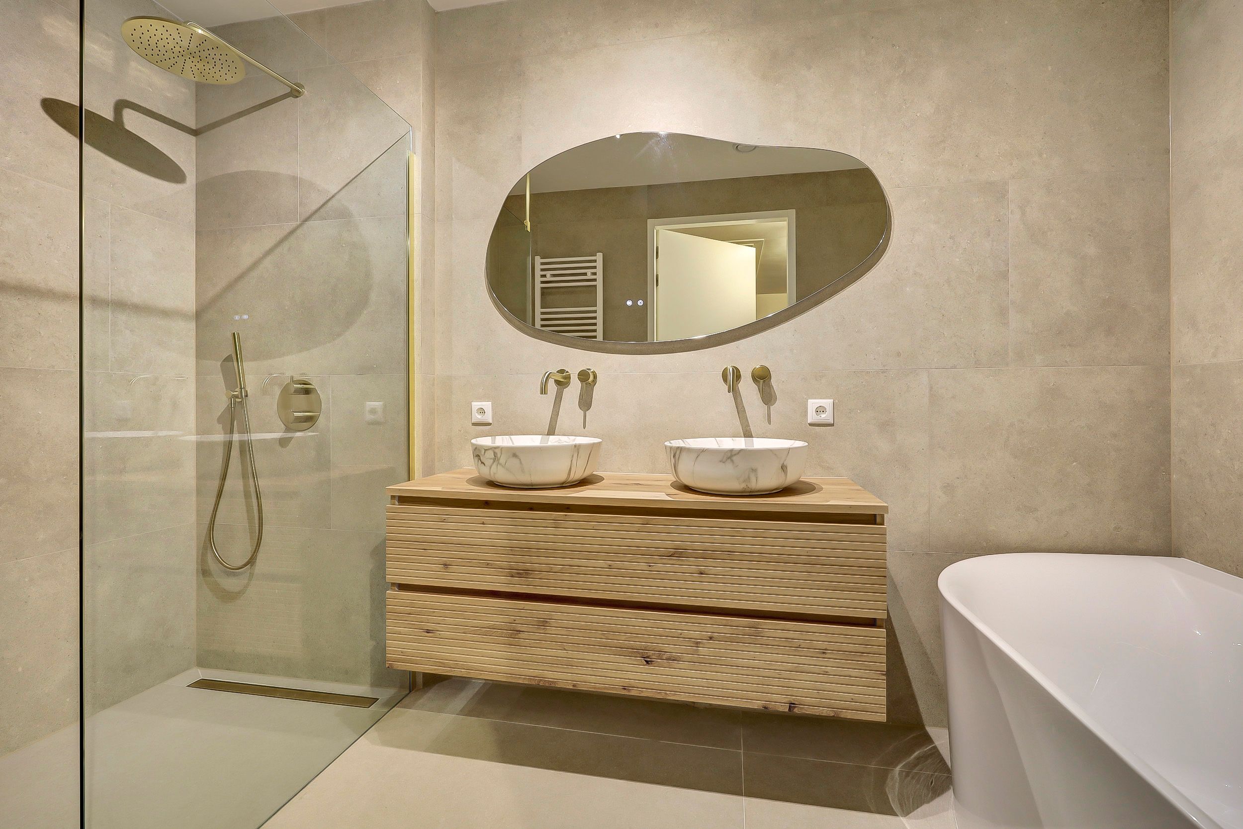 Badkamer van Henry uit Riethoven met beige marmerlook tegels, eiken badmeubel en messing kranen