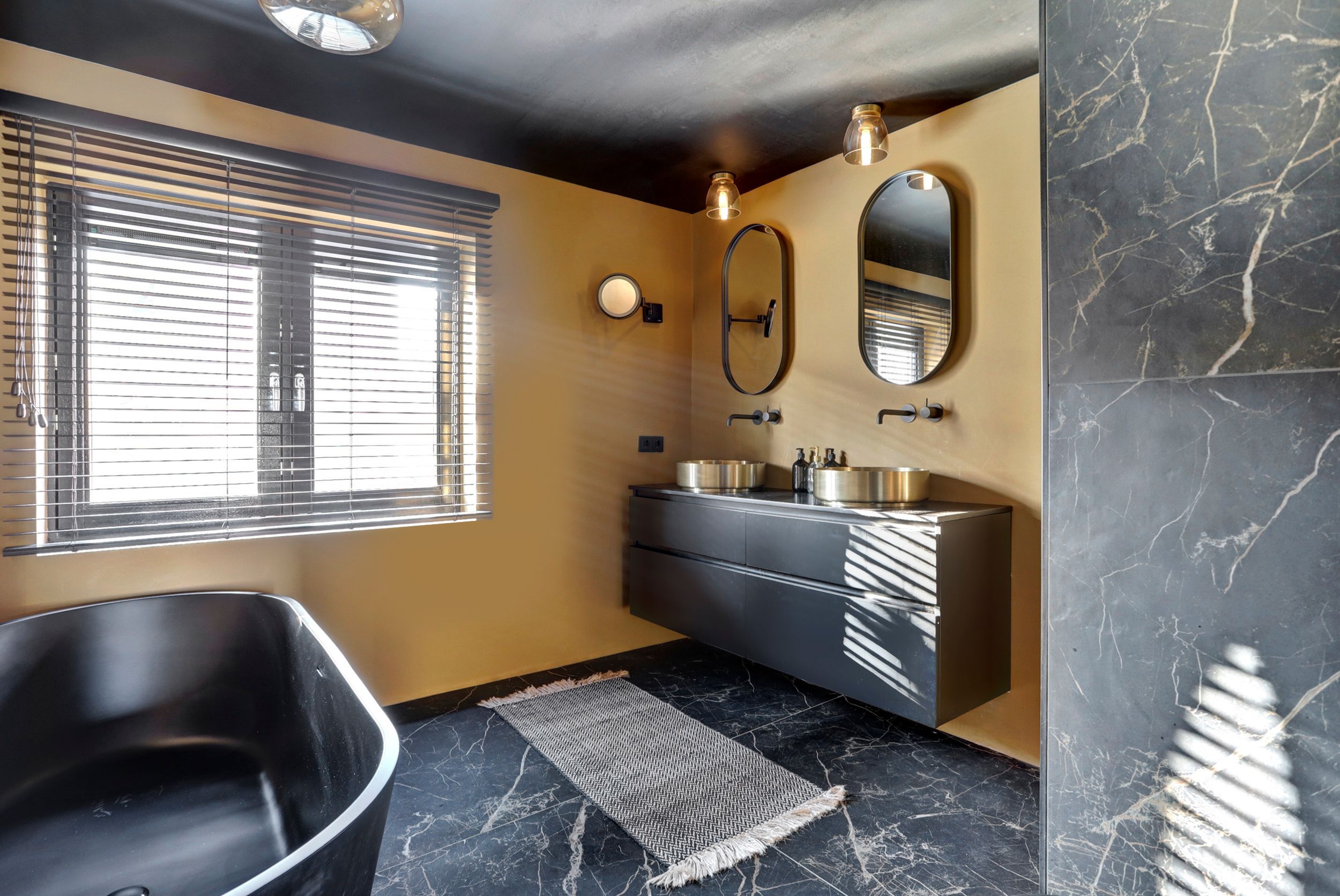 Badkamer van Melissa uit Tilburg met donkere marmerlook, gouden wanden en mat zwart ligbad