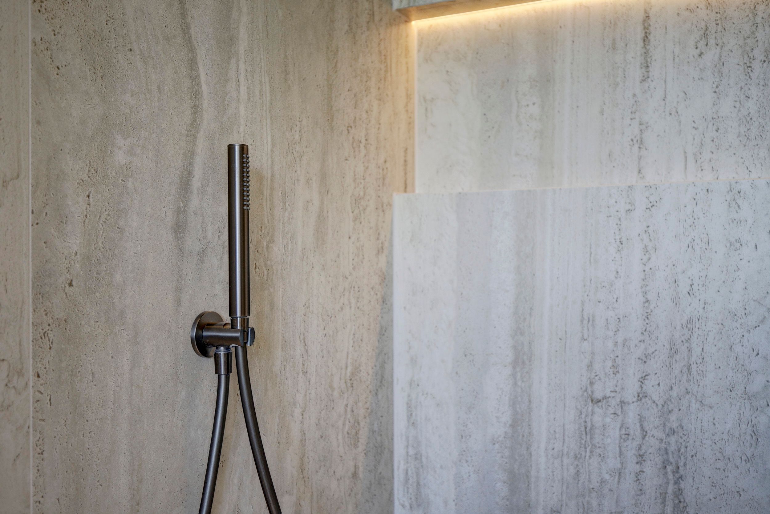 Handdouche aan wandaansluitbocht in gunmetal op travertin-look wand